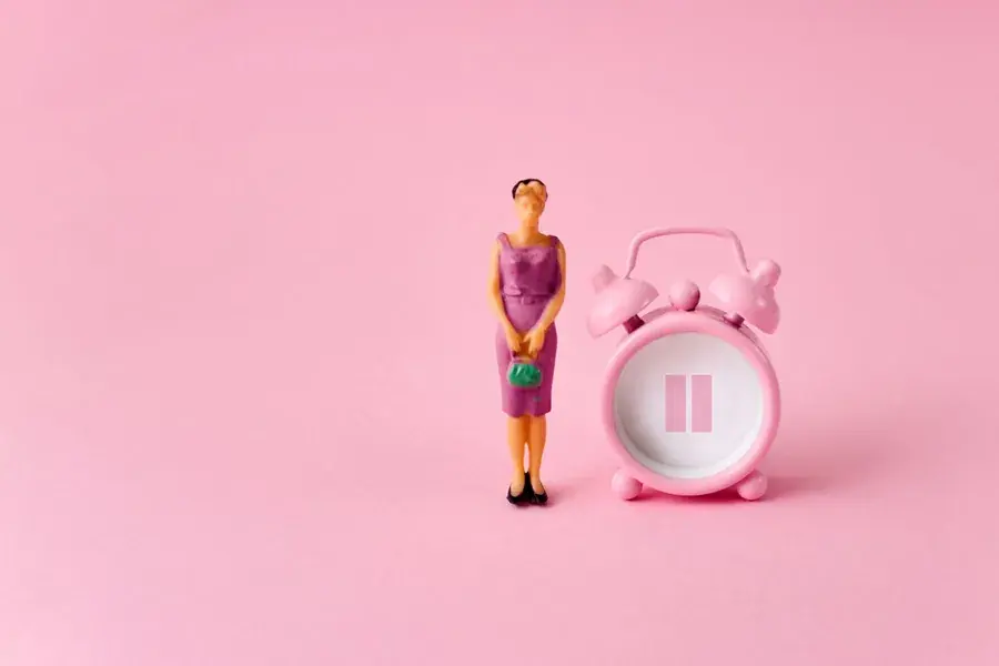 Miniature woman beside a pink alarm clock on a pink background